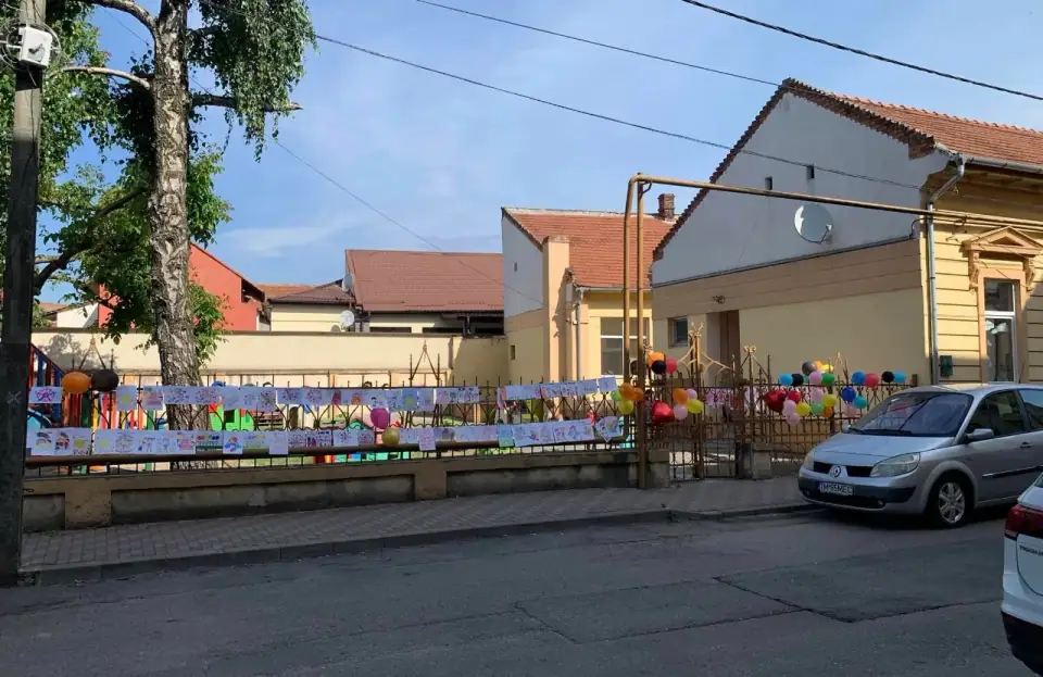 Gardul grădiniței, plin cu desene ale copiilor și baloane colorate, la marginea străzii